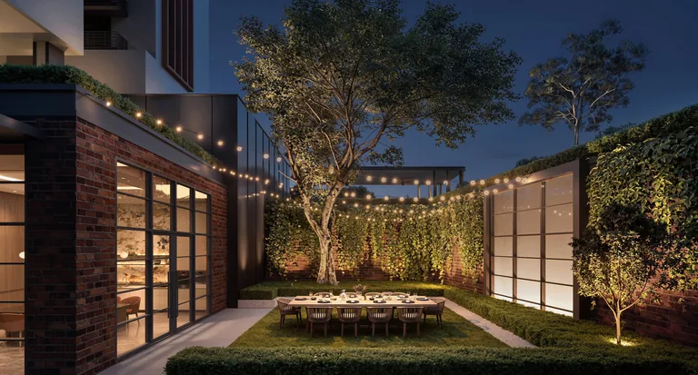 Hudson Place Residences, artist&rsquo;s impression: the Courtyard Garden at dusk, a long dining table on the lawn under a tree, with strings of lights between brick and glass walls